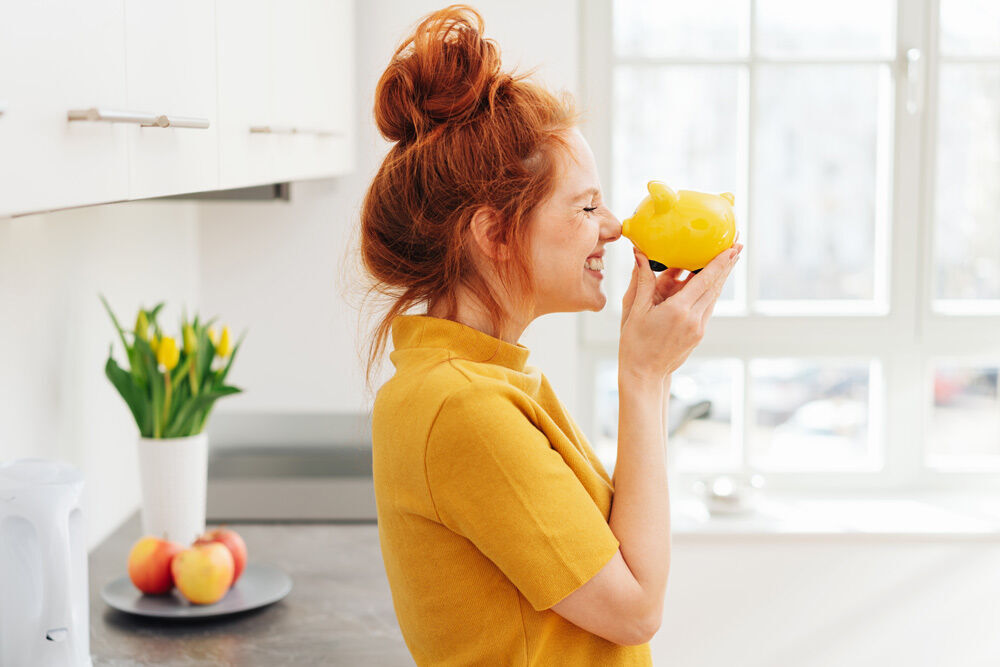 eine Frau, die ein gelbes Sparschwein mit der Nase anstupst