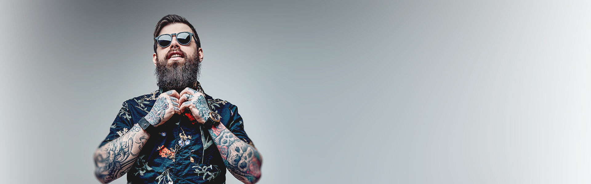 Bärtiger Mann mit Sonnenbrille und tätowierten Armen im bunten kurzärmeligen Hemd bereitet sich auf sein Coaching für Personen mit individuellen Anliegen vor.