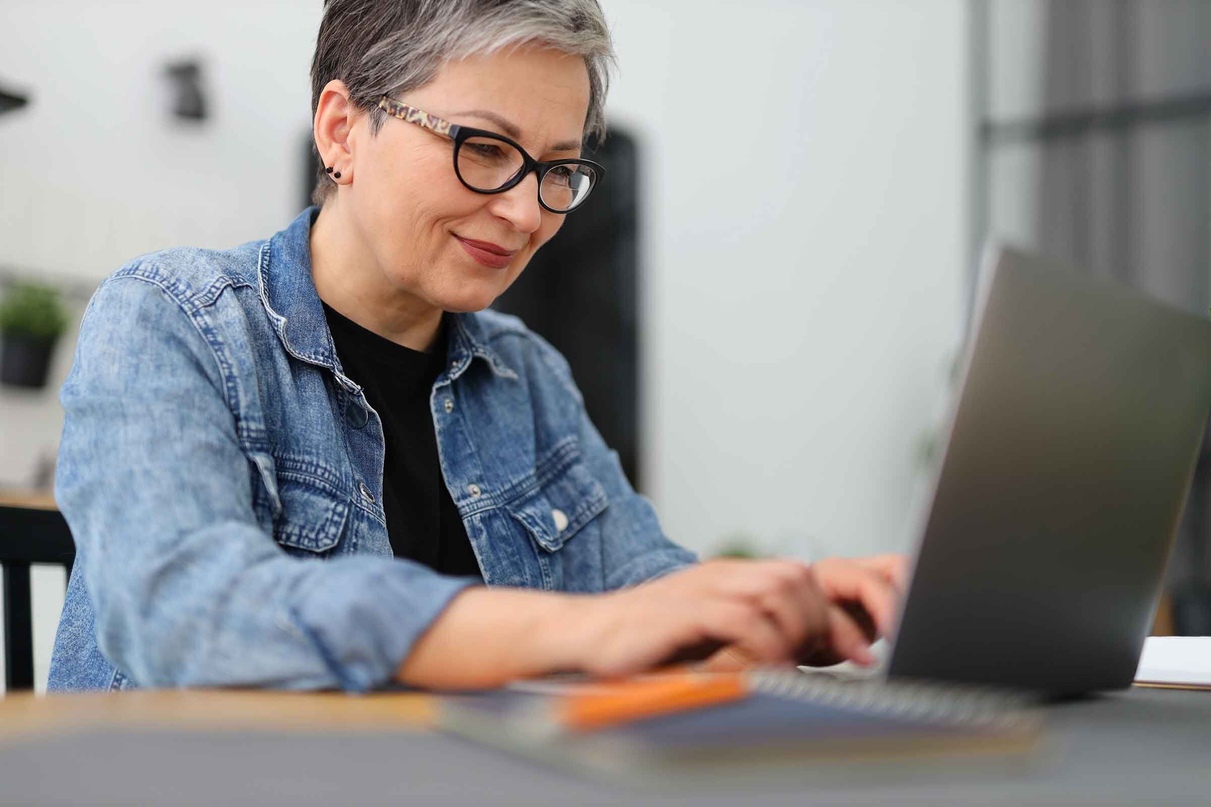 eine Frau sitzt an einem Tisch mit einem Laptop vor orangenem Hintergrund